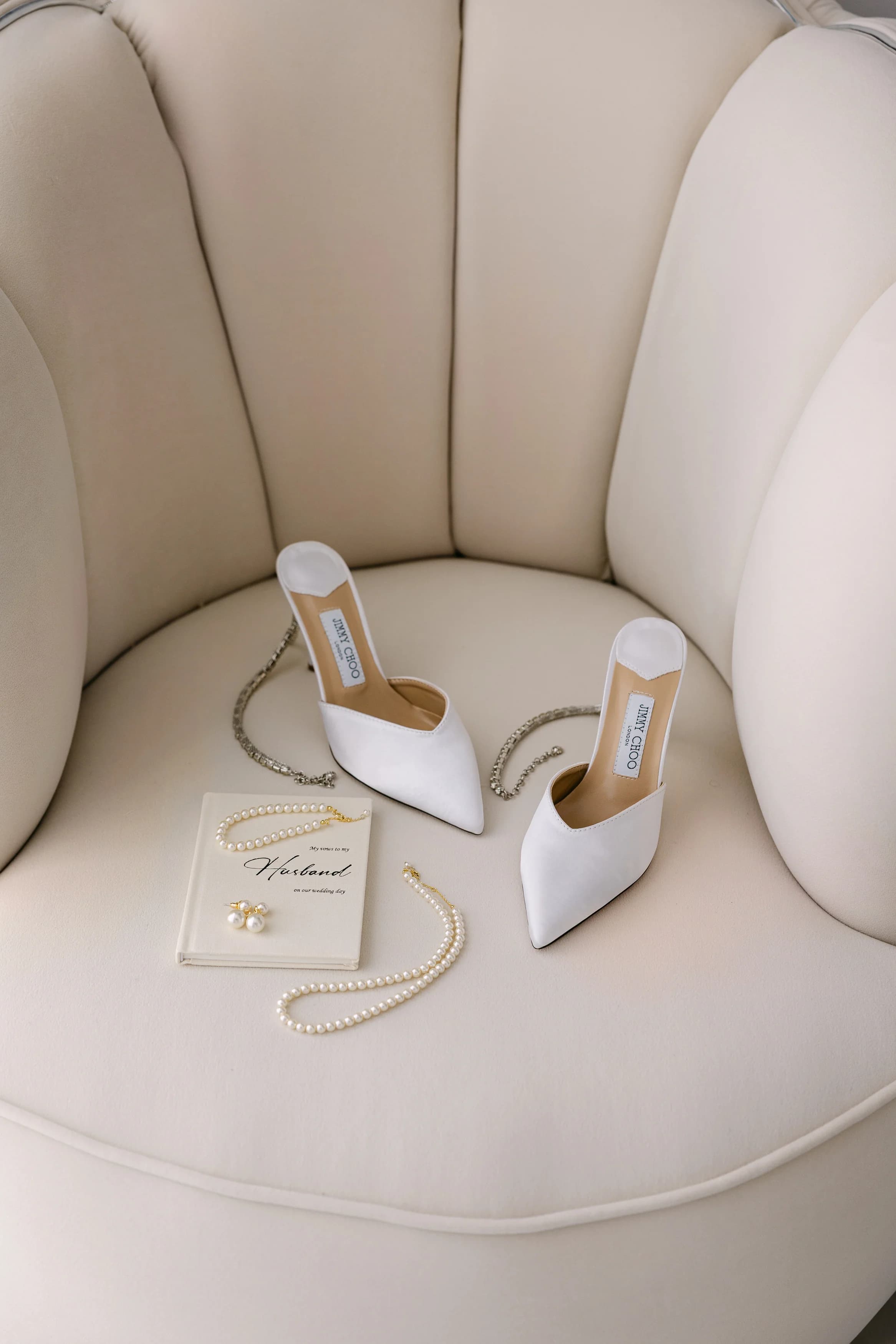 Bridal shoes, pearls, and earrings styled on a cream lounge chair before the wedding.