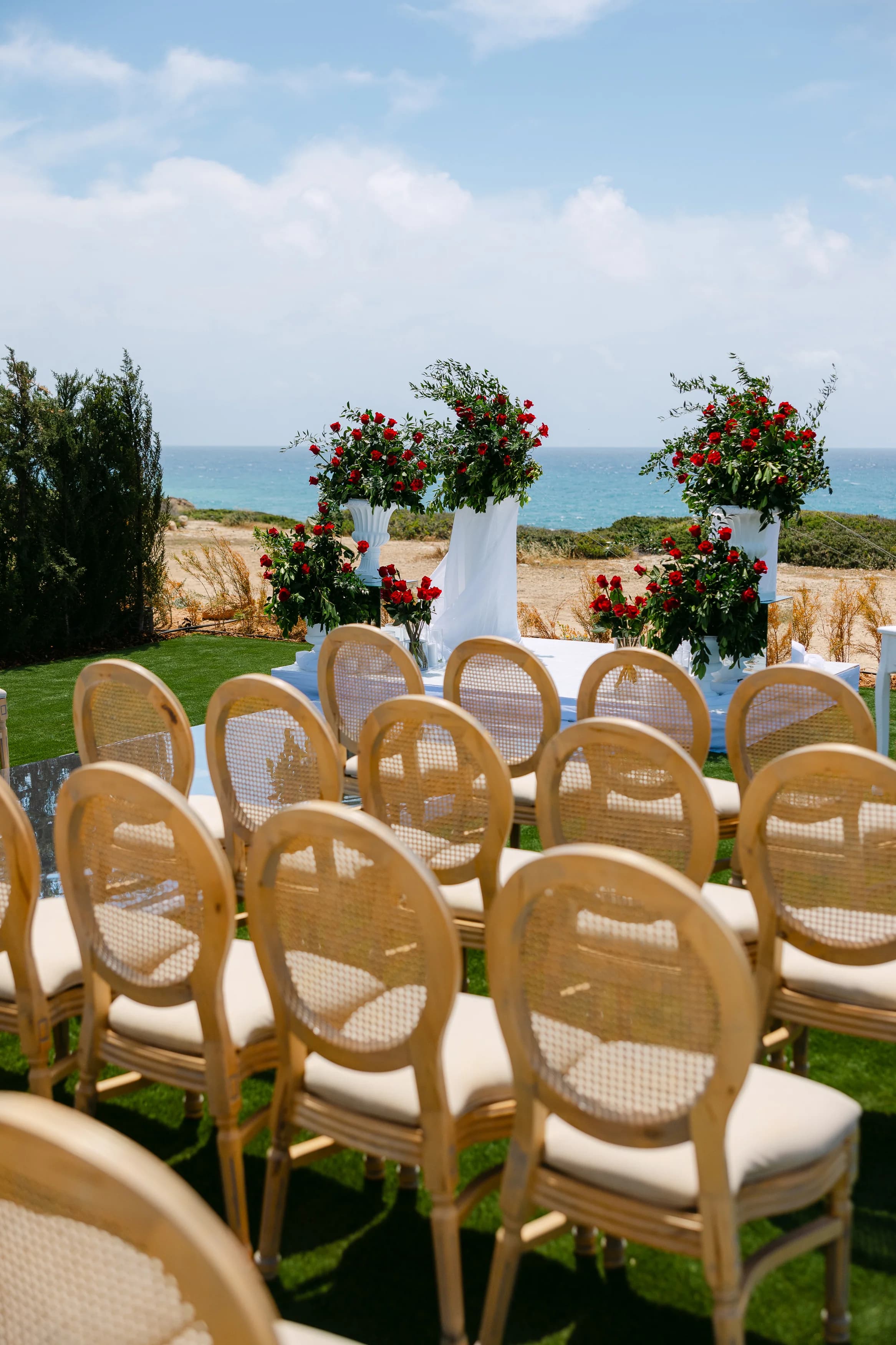 Cane-back ceremony chairs and floral arrangements at Ozea framed by the Mediterranean.