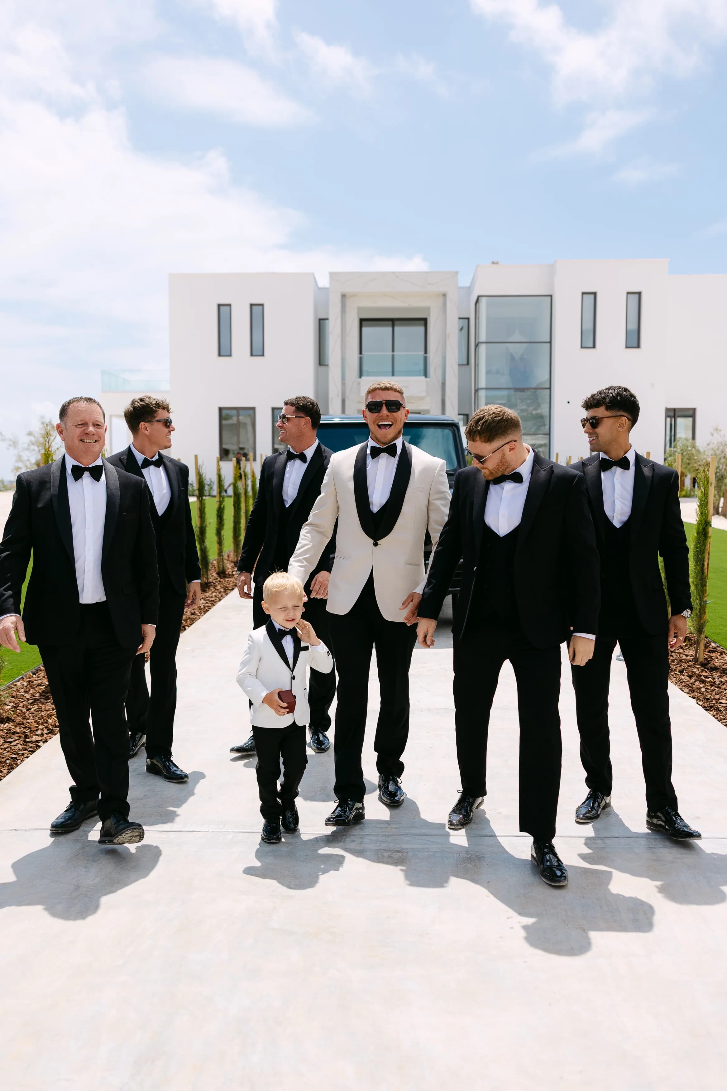 Groom and groomsmen walking together on the venue driveway at OZEA with the young ring bearer.