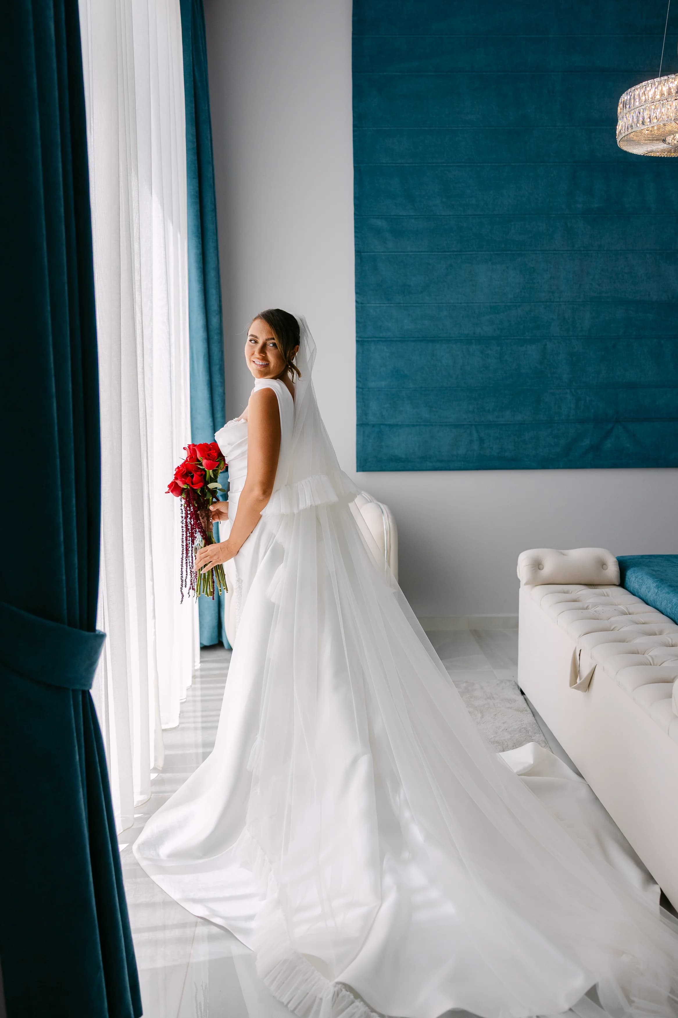 Bride in her gown holding a red bouquet inside the bridal suite at OZEA.