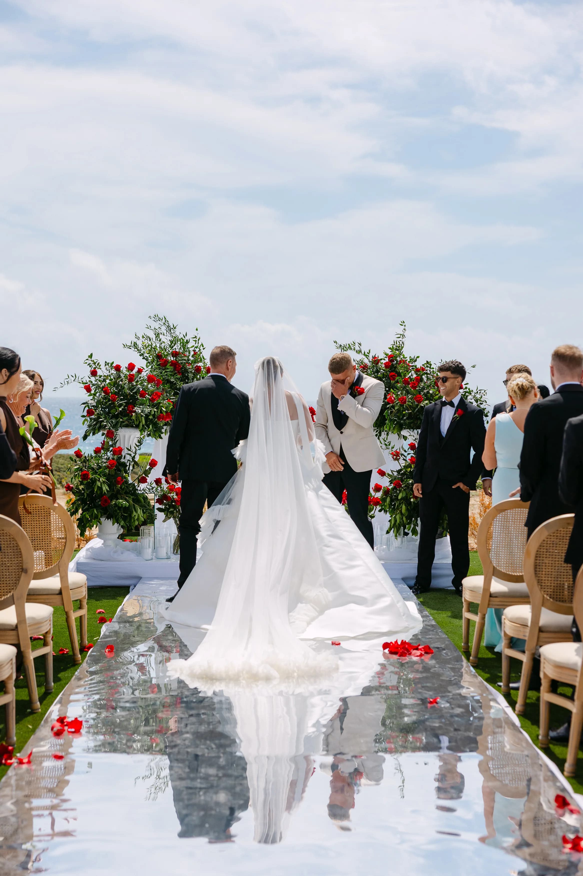 Bride approaching the altar at Ozea with red rose petals along the mirrored aisle.