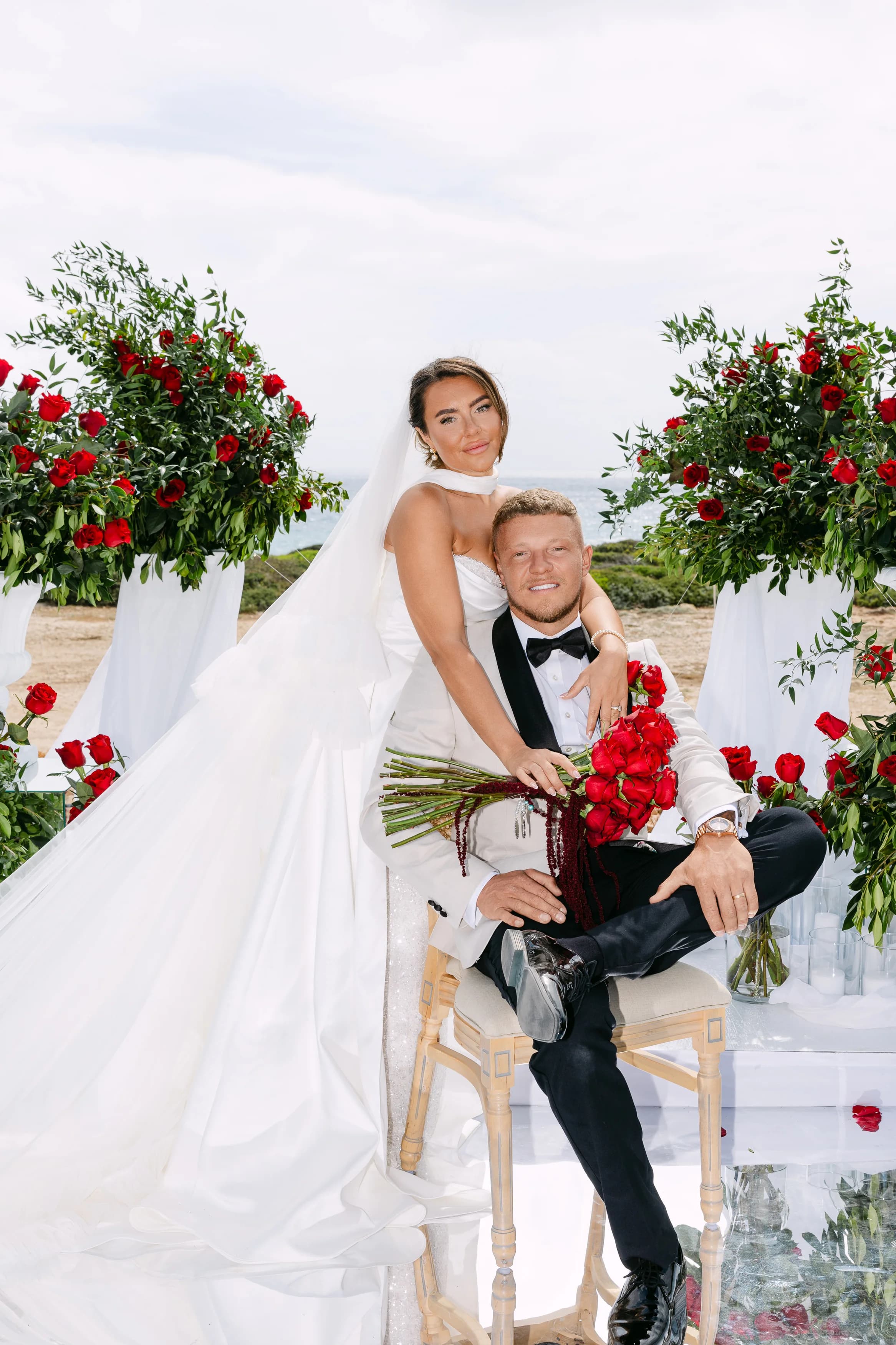 Bride embracing the groom at the altar at Ozea framed by red roses and the sea.