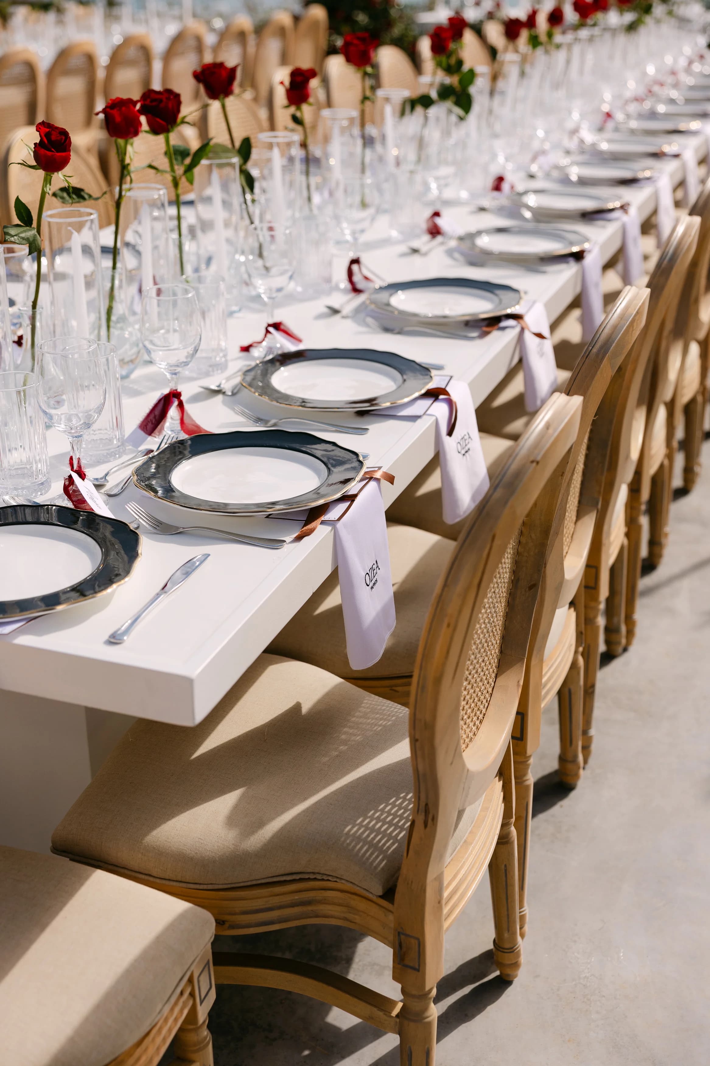 Close view of a long banquet table at Ozea with grey-rimmed plates, red rose buds, and personalised place cards.