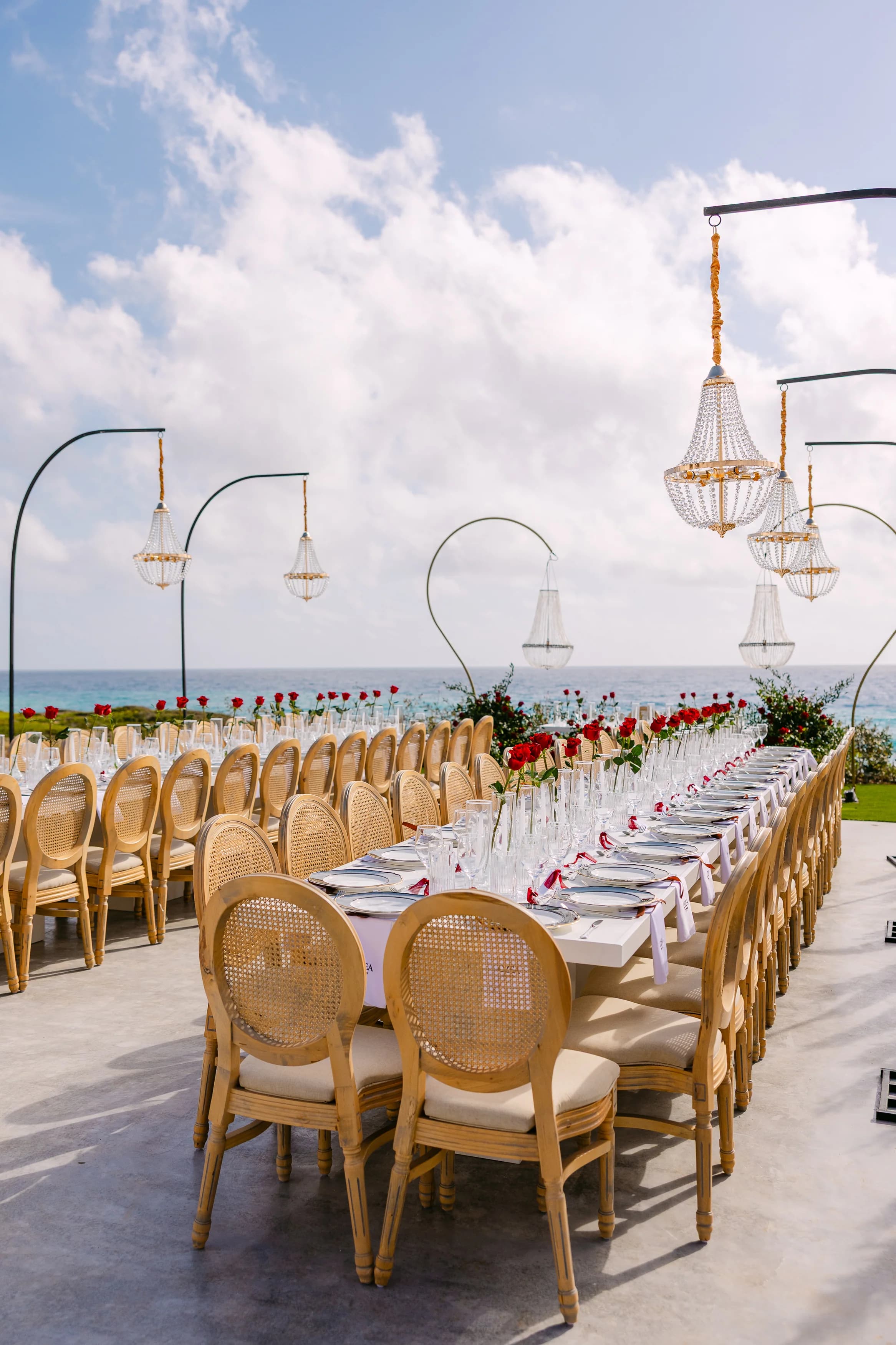 Long banquet table set for a wedding reception at OZEA with crystal chandeliers and a sea-view backdrop.