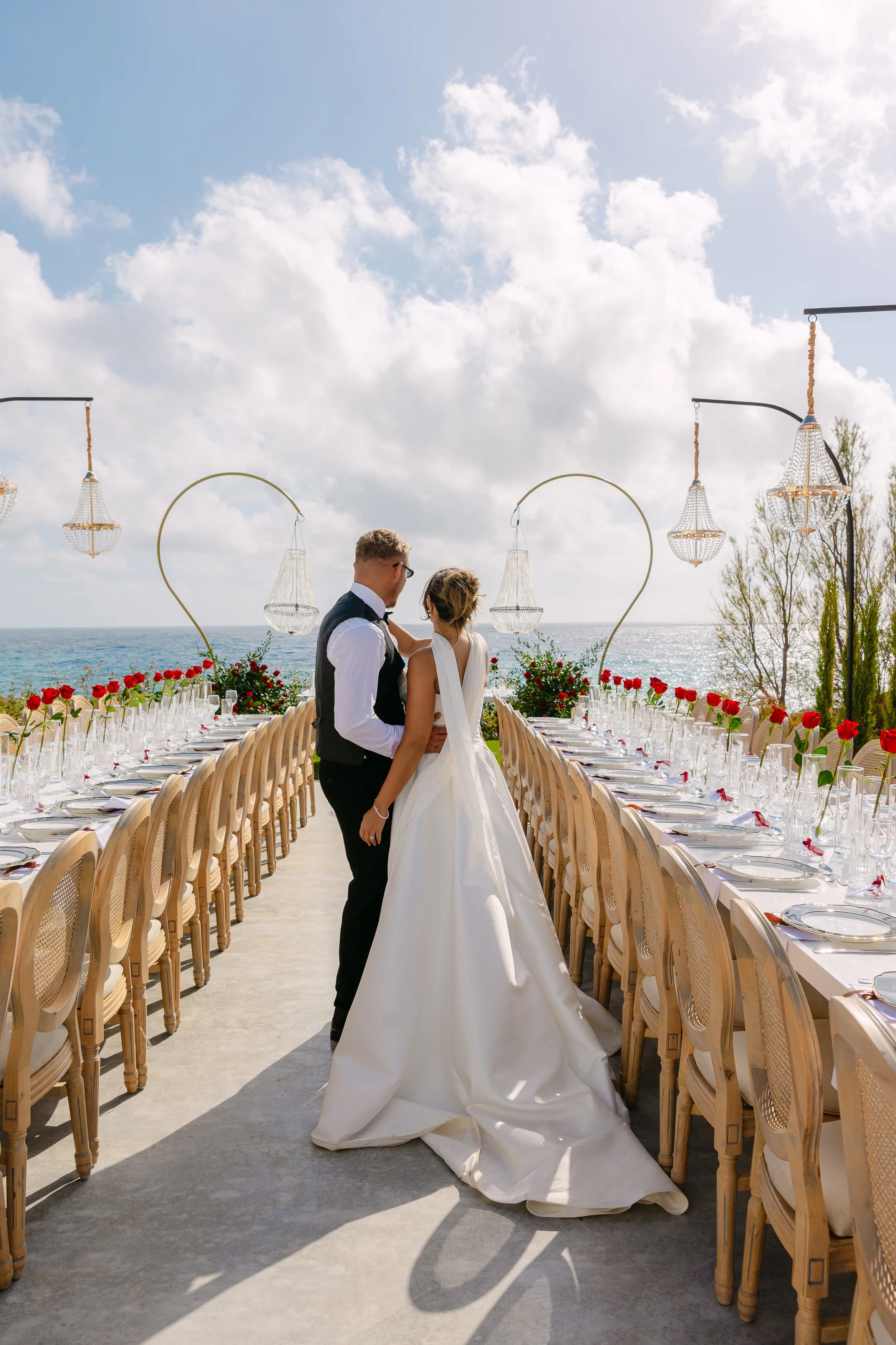 Bride and groom standing at the head of the banquet table at Ozea, looking toward the Mediterranean.