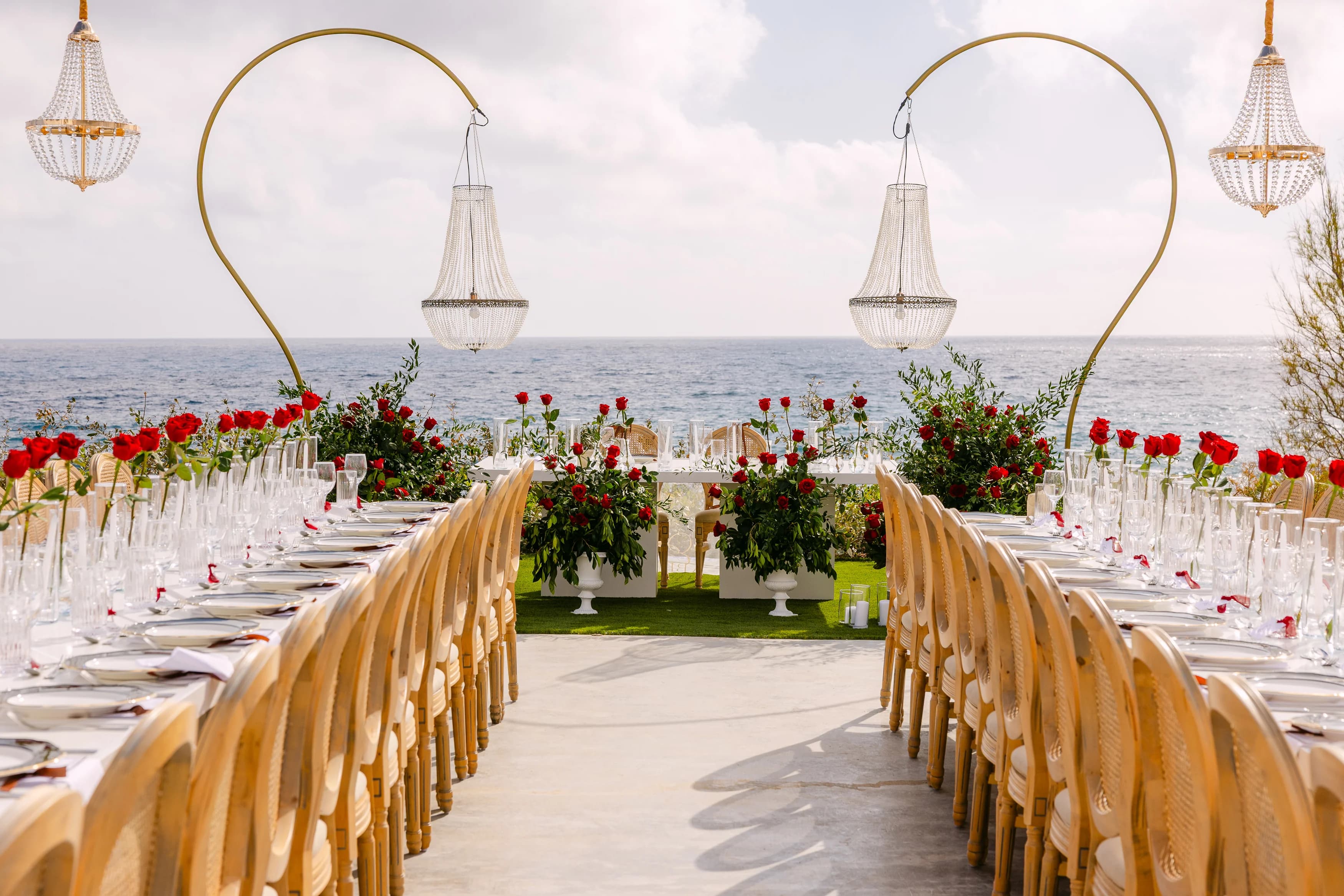 Long banquet tables at Ozea framed by tall arched chandelier stands and the Mediterranean.