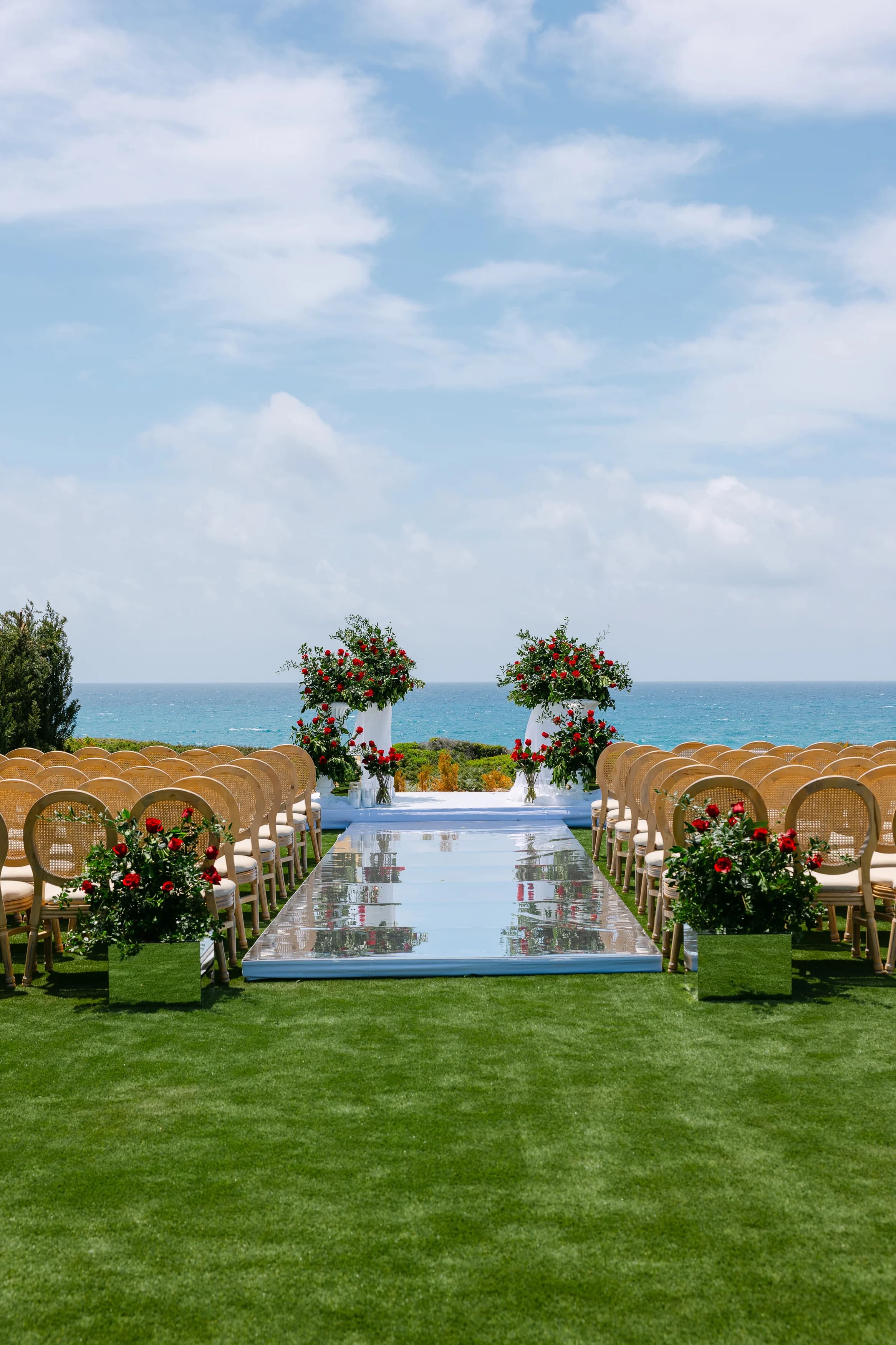 Vertical ceremony aisle view at Ozea with floral arrangements and the sea ahead.