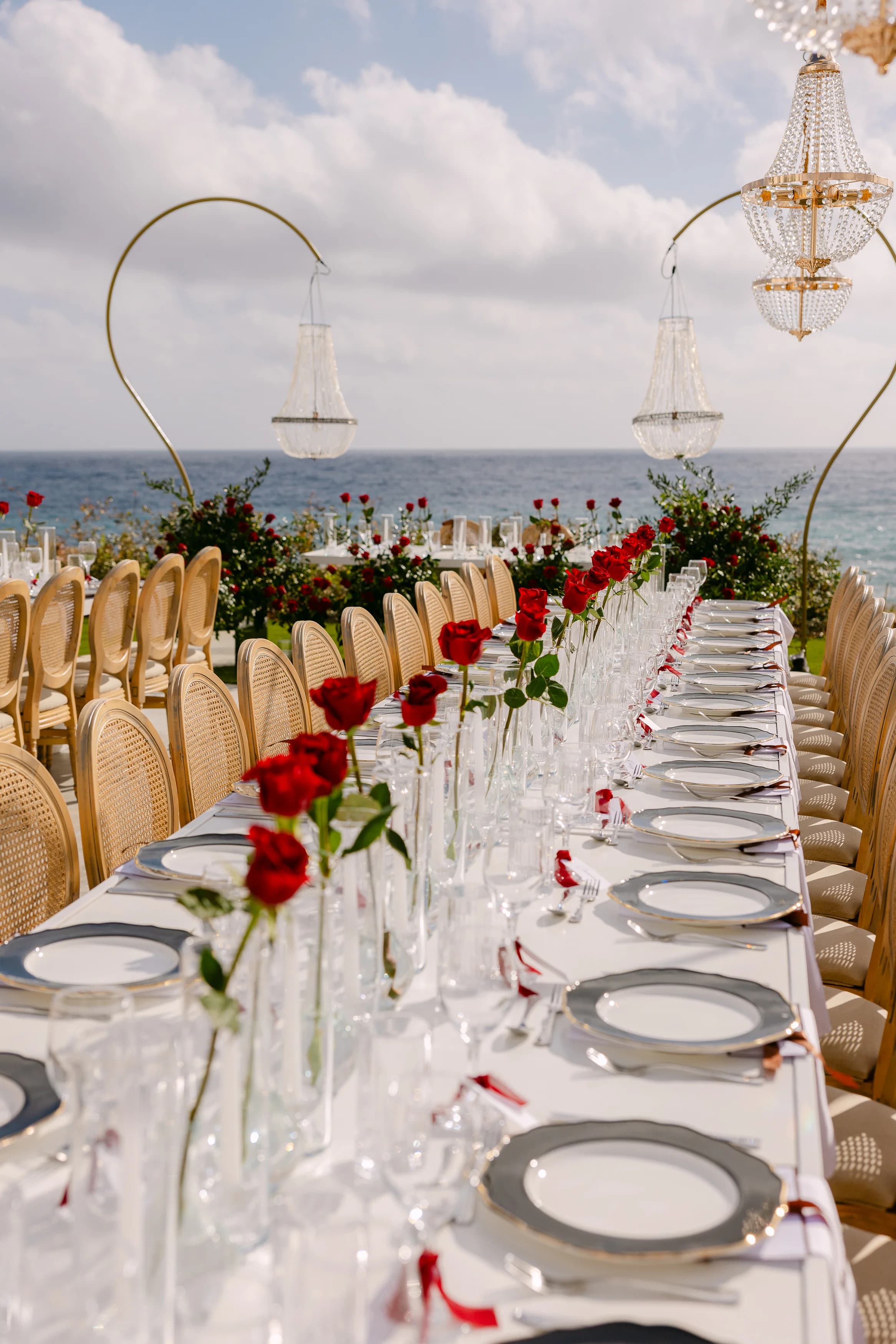 Vertical view of the long banquet table at OZEA with chandeliers, single roses, and the sea behind.