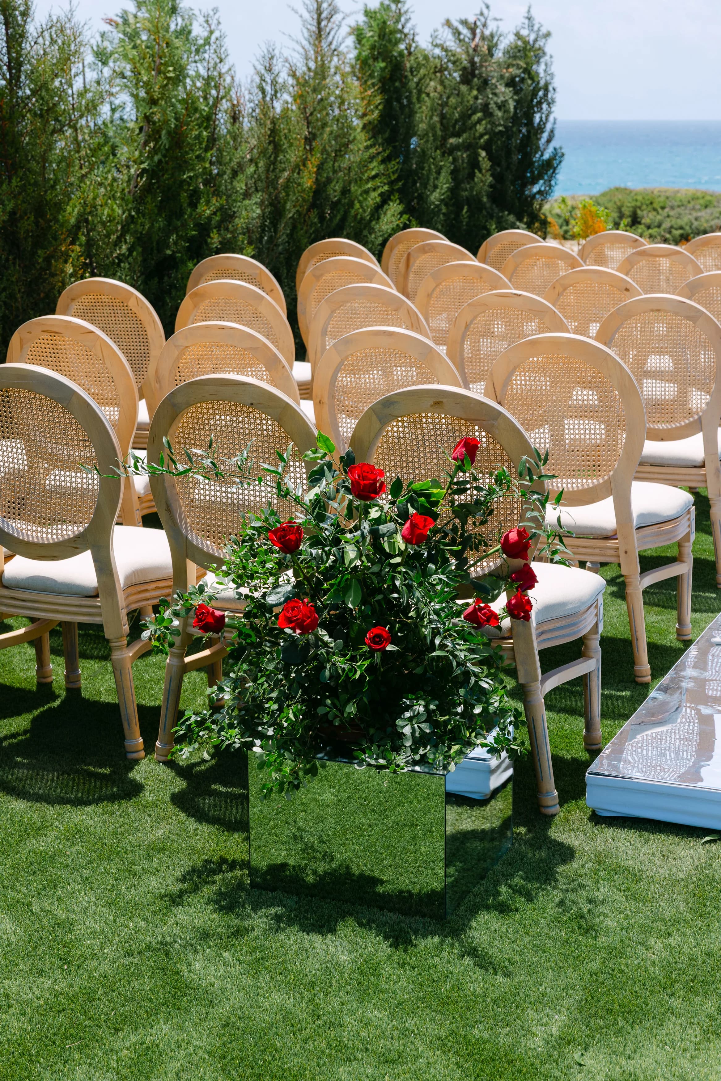 Close view of ceremony chairs with red rose arrangements on a mirrored cube at Ozea.