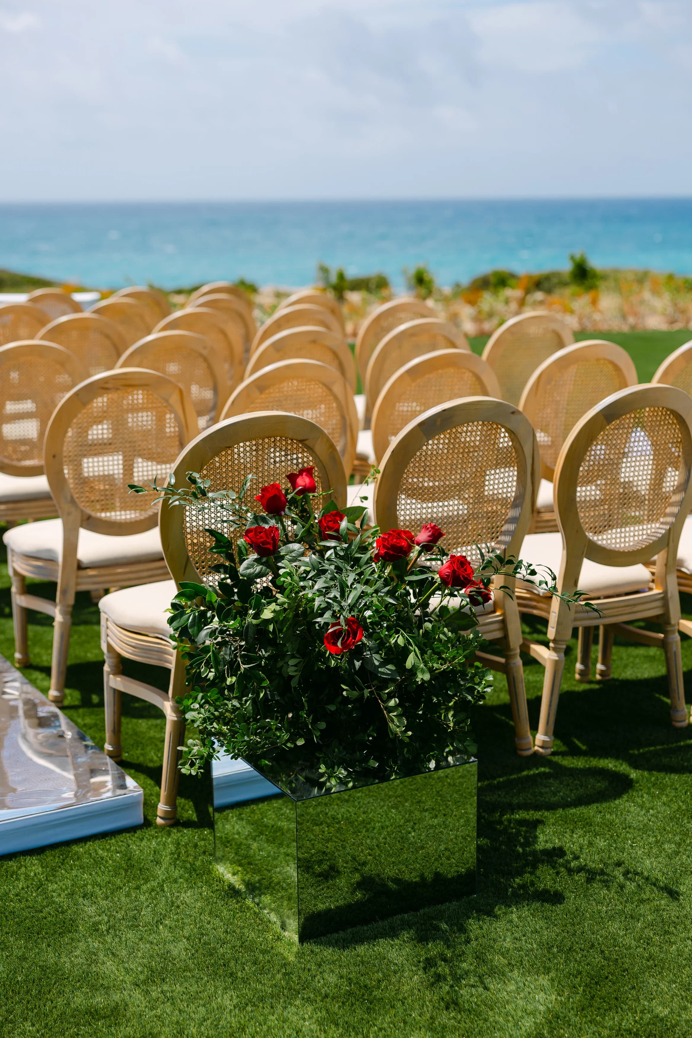 Ceremony chairs at Ozea with a red rose arrangement on a mirrored cube and the sea behind.
