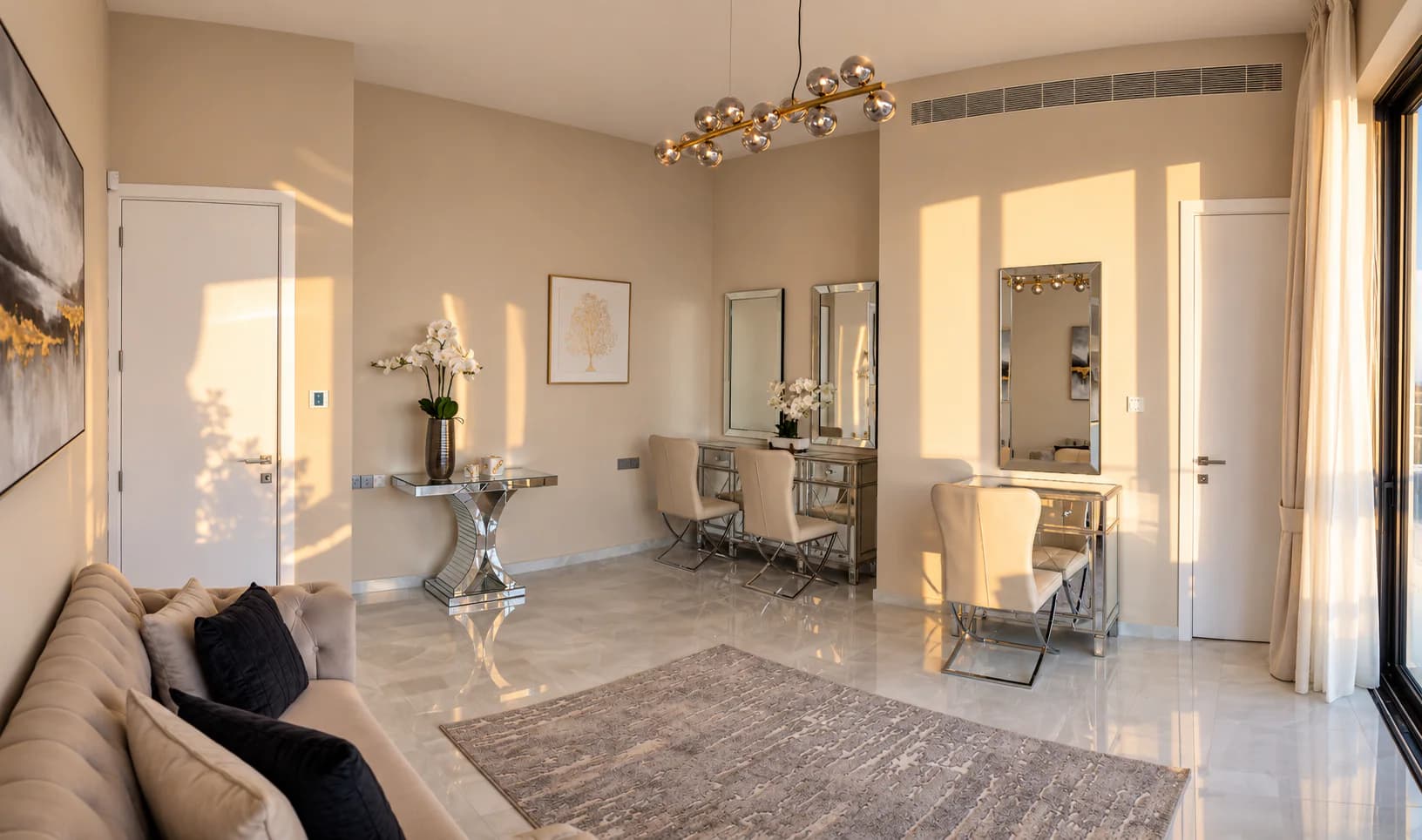 The dressing room of the bridal suite at OZEA with mirrored vanity stations and cream chairs, a mirrored console with white orchids, a tufted sofa, and late sun across the marble floor.